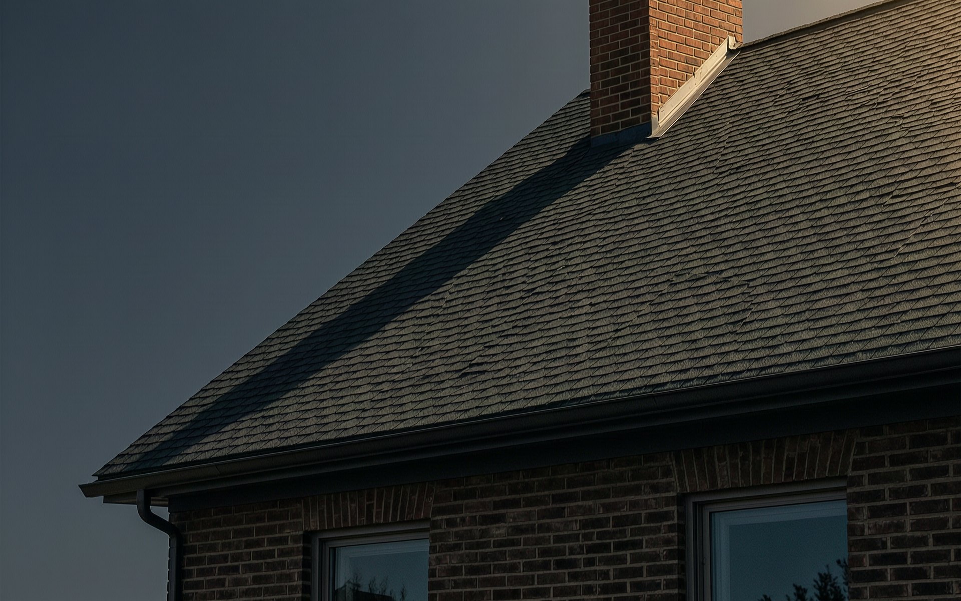 A shingled roof and brick chimney at dusk